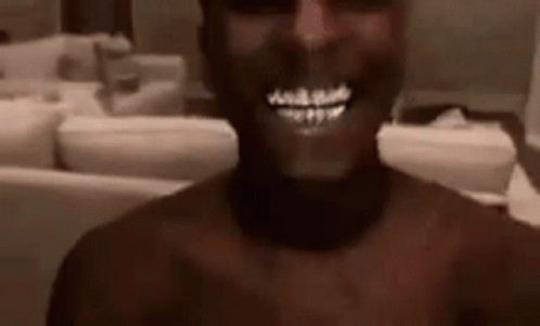 A Man Without A Shirt Is Smiling In A Living Room . GIF
