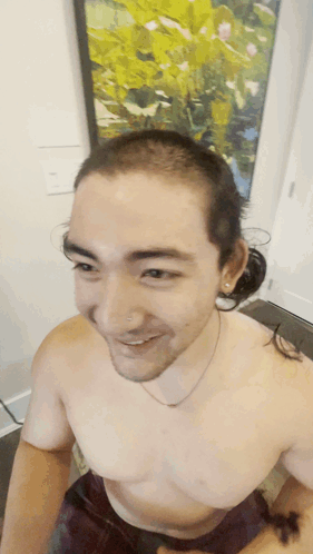 A Man Without A Shirt Is Smiling In Front Of A Picture GIF