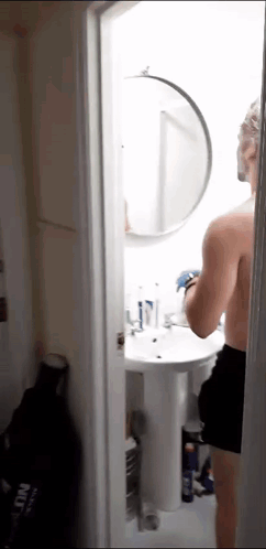 A Man Without A Shirt Is Standing In A Bathroom Looking At Himself In A Mirror GIF