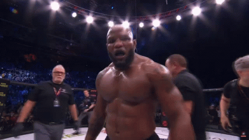 A Man Without A Shirt Is Standing In A Boxing Ring With A Referee Behind Him GIF