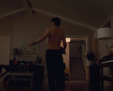 A Man Without A Shirt Is Standing In A Dark Room GIF
