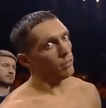 A Man Without A Shirt Is Standing In A Dark Room With A Man In The Background . GIF