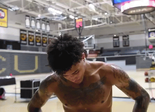 a man without a shirt is standing in a gym with a sign that says u on it