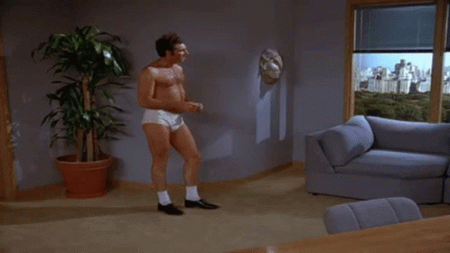 A Man Without A Shirt Is Standing In A Living Room GIF