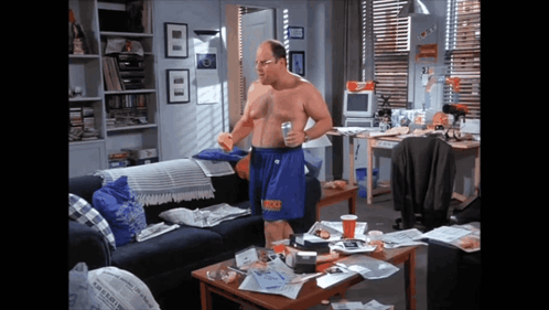 A Man Without A Shirt Is Standing In A Living Room With A Newspaper On The Coffee Table GIF