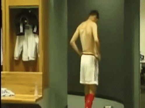 A Man Without A Shirt Is Standing In A Locker Room With A Towel Around His Waist . GIF