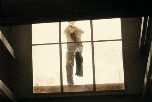 A Man Without A Shirt Is Standing In A Window GIF