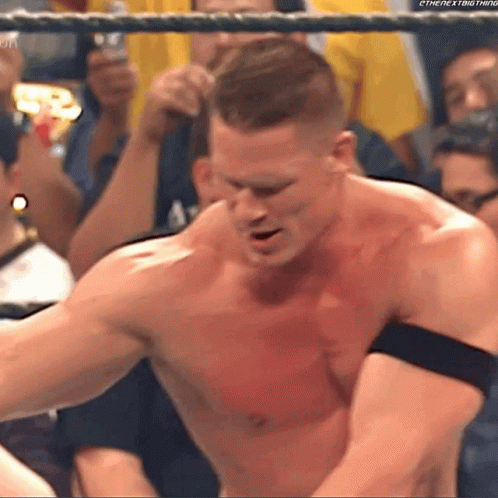 A Man Without A Shirt Is Standing In A Wrestling Ring With A Crowd Behind Him . GIF