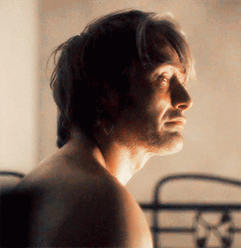 A Man Without A Shirt Is Standing In Front Of A Bed Looking At The Camera . GIF