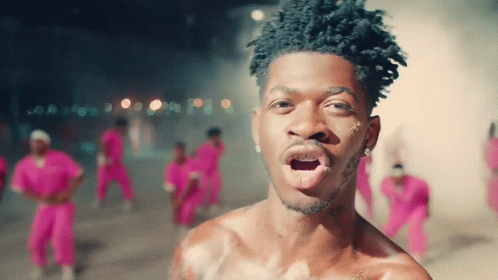 A Man Without A Shirt Is Standing In Front Of A Crowd Of People In Pink Pants GIF