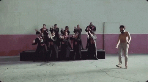 A Man Without A Shirt Is Standing In Front Of A Group Of People Dancing In A Room . GIF