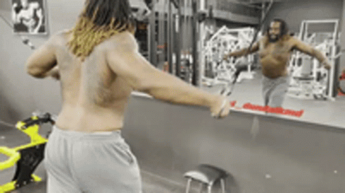 A Man Without A Shirt Is Standing In Front Of A Mirror In A Gym GIF