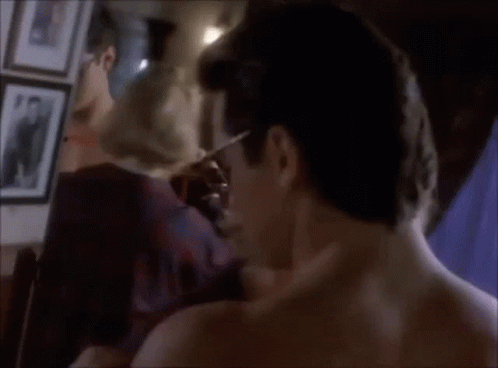 A Man Without A Shirt Is Standing In Front Of A Mirror Looking At His Reflection GIF