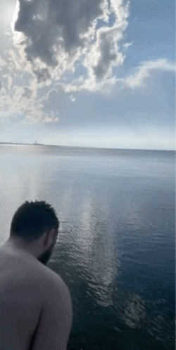 A Man Without A Shirt Is Standing In The Water Looking At The Ocean GIF