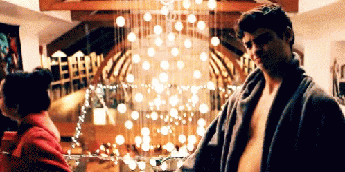 A Man Without A Shirt Is Standing Next To A Woman In A Room With A Christmas Tree In The Background . GIF