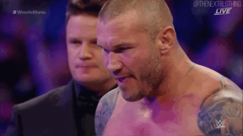 A Man Without A Shirt Is Standing Next To Another Man In A Wrestling Match . GIF