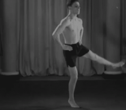 A Man Without A Shirt Is Standing On One Leg On A Stage In A Black And White Photo . GIF