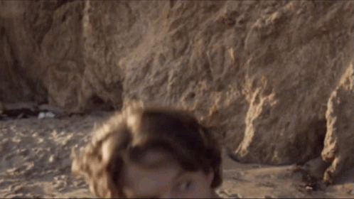 A Man Without A Shirt Is Standing On The Beach Looking At The Camera GIF