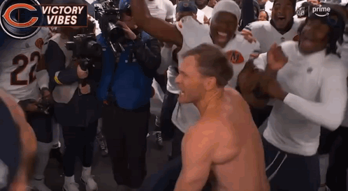 A Man Without A Shirt Is Surrounded By A Group Of Players And A Banner That Says Victory Vibes GIF