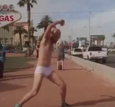 A Man Without A Shirt Is Throwing A Ball In Front Of A Sign That Says Gas GIF