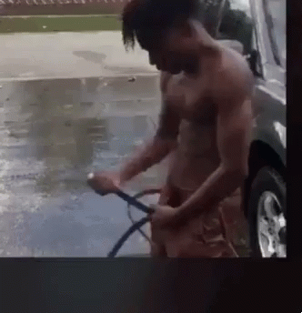 A Man Without A Shirt Is Washing A Car With A Hose . GIF