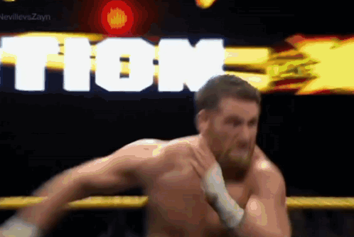 A Man Without A Shirt Is Wrestling In A Ring With The Word Tion Behind Him . GIF