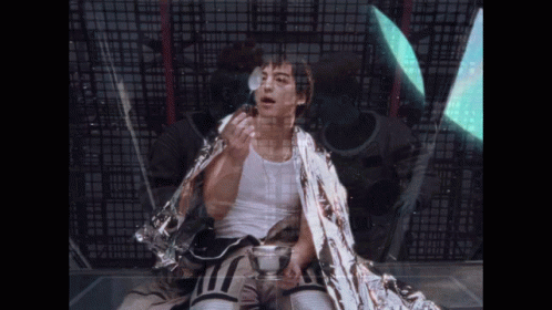 A Man Wrapped In A Silver Blanket Holds A Cup GIF