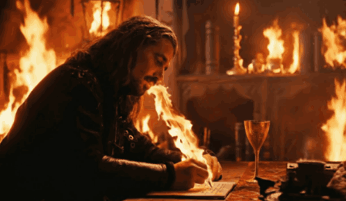 A Man Writes On A Piece Of Paper In Front Of A Fireplace With Flames Coming Out Of His Mouth GIF