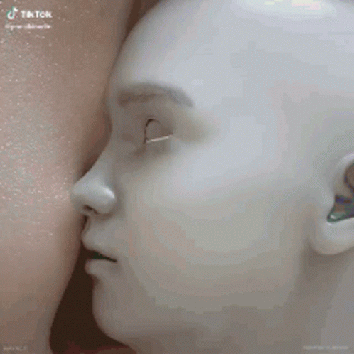 A Mannequin With Its Mouth Open Is Being Breastfed By A Woman . GIF
