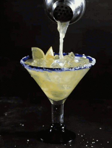A Margarita Is Being Poured Into A Martini Glass With Ice GIF