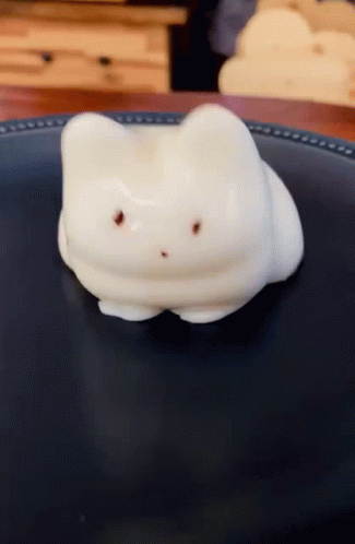 A Marshmallow In The Shape Of A Cat Laying On A Black Plate GIF