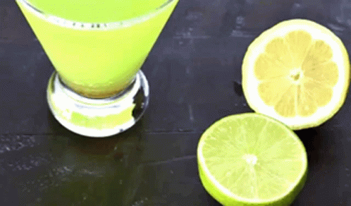 A Martini Glass Filled With A Yellow Liquid Next To Two Sliced Limes GIF