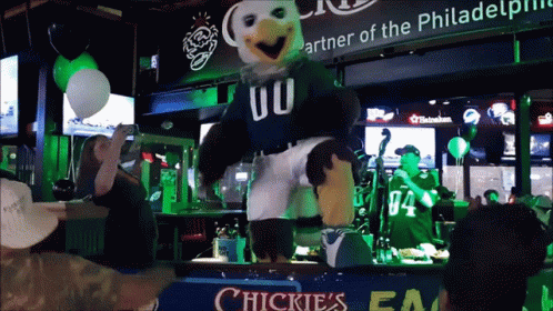 A Mascot Dancing In Front Of A Sign That Says Chickies GIF