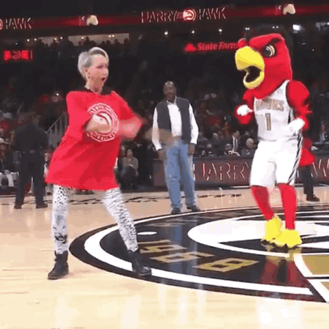 A Mascot For The Hawks Is Dancing With A Woman On A Basketball Court GIF