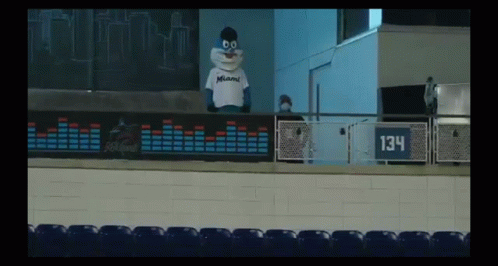 A Mascot For The Miami Dolphins Is Standing On A Balcony In A Stadium . GIF