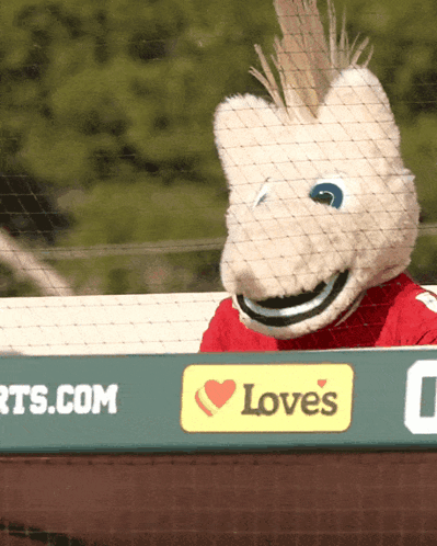 A Mascot Is Behind A Sign That Says Love 'S On It GIF