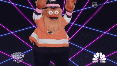 A Mascot Is Dancing In Front Of A Glowing Background That Says Nbc GIF