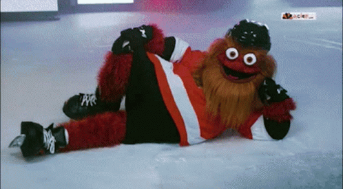 A Mascot Is Laying On The Ice Wearing A Hat And Gloves GIF