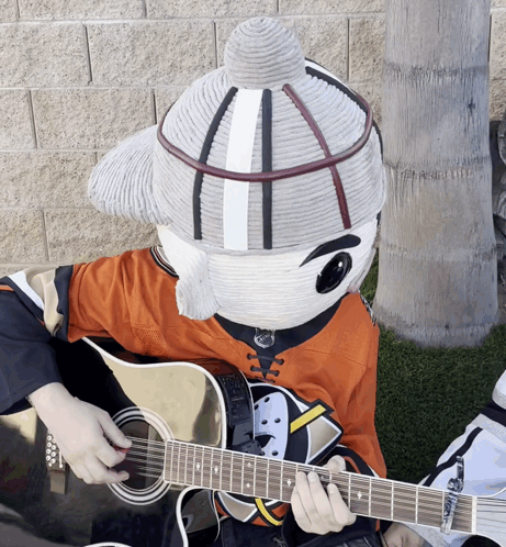 A Mascot Is Playing A Guitar And Wearing An Orange Shirt GIF