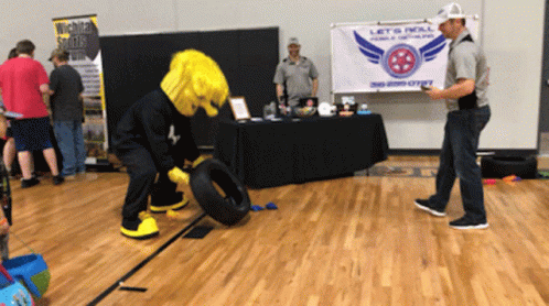 a mascot is rolling a tire in front of a sign that says let 's roll