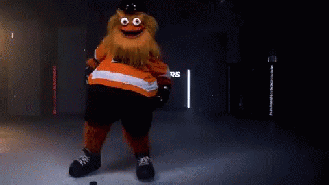A Mascot Is Standing On A Ice Rink With A Puck In His Hand . GIF