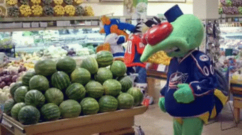 A Mascot Standing In Front Of A Display Of Watermelons GIF