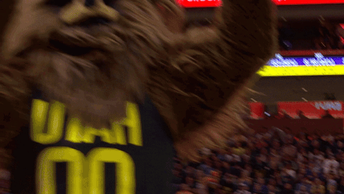 A Mascot Wearing A Utah Jersey Stands In Front Of A Crowd At A Basketball Game GIF