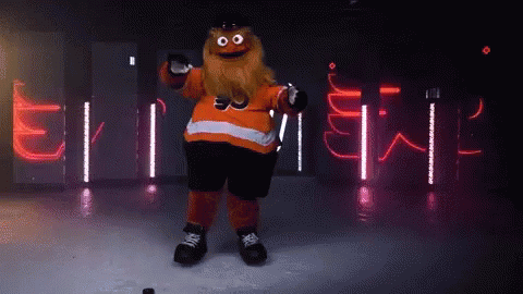 A Mascot With A Beard Is Holding A Hockey Puck In Front Of A Sign That Says ' Flyers ' GIF
