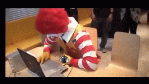 A Mcdonald 'S Clown Is Sitting At A Table Using A Laptop Computer GIF