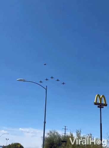 A Mcdonald 'S Sign Is In The Foreground Of A Group Of Planes In The Sky GIF