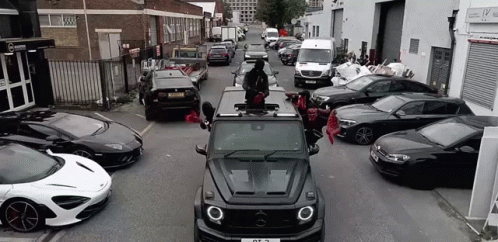 A Mercedes Benz G63 Is Driving Down A Street Surrounded By Lots Of Cars . GIF