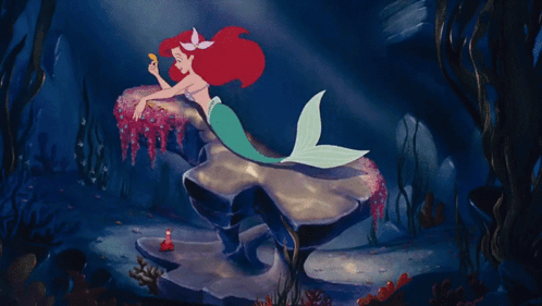 A Mermaid Is Laying On A Rock In The Ocean GIF