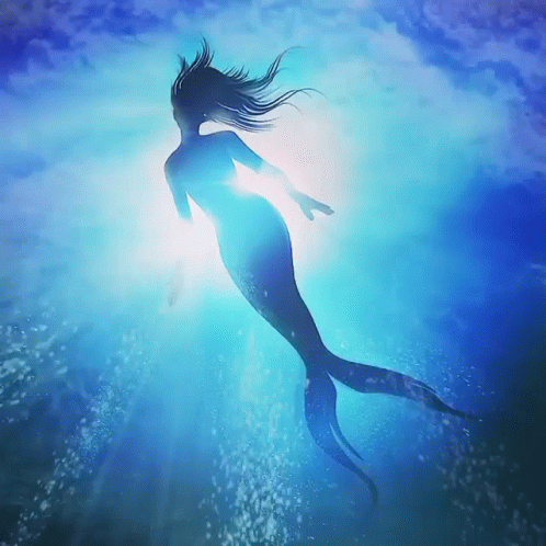 A Mermaid Is Swimming In The Ocean With The Sun Shining Through The Water GIF