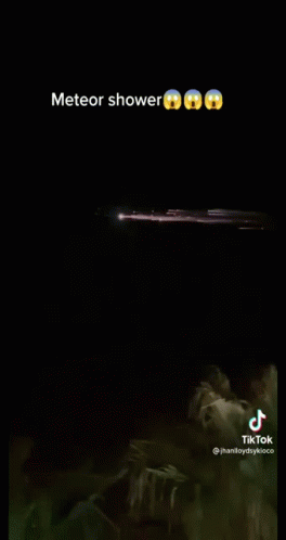 A Meteor Shower Is Visible In The Night Sky Over A Body Of Water . GIF